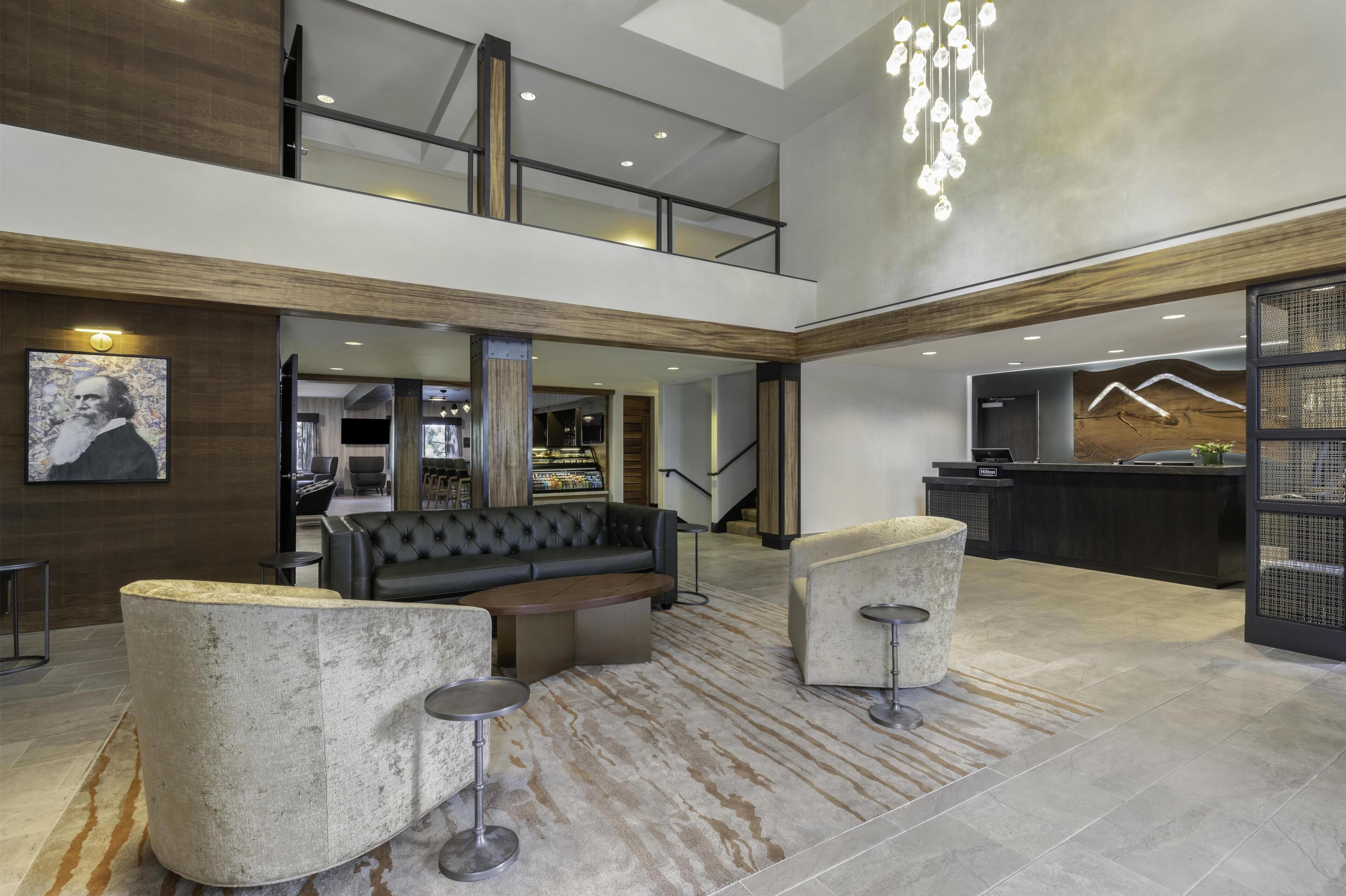A spacious lobby with a high ceiling, a black leather sofa, a round coffee table, and a reception desk.