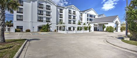 A multi-story hotel with a central courtyard, a covered entrance, and a parking area.