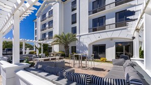 A modern outdoor seating area with striped sofas and tables, surrounded by a white pergola structure.