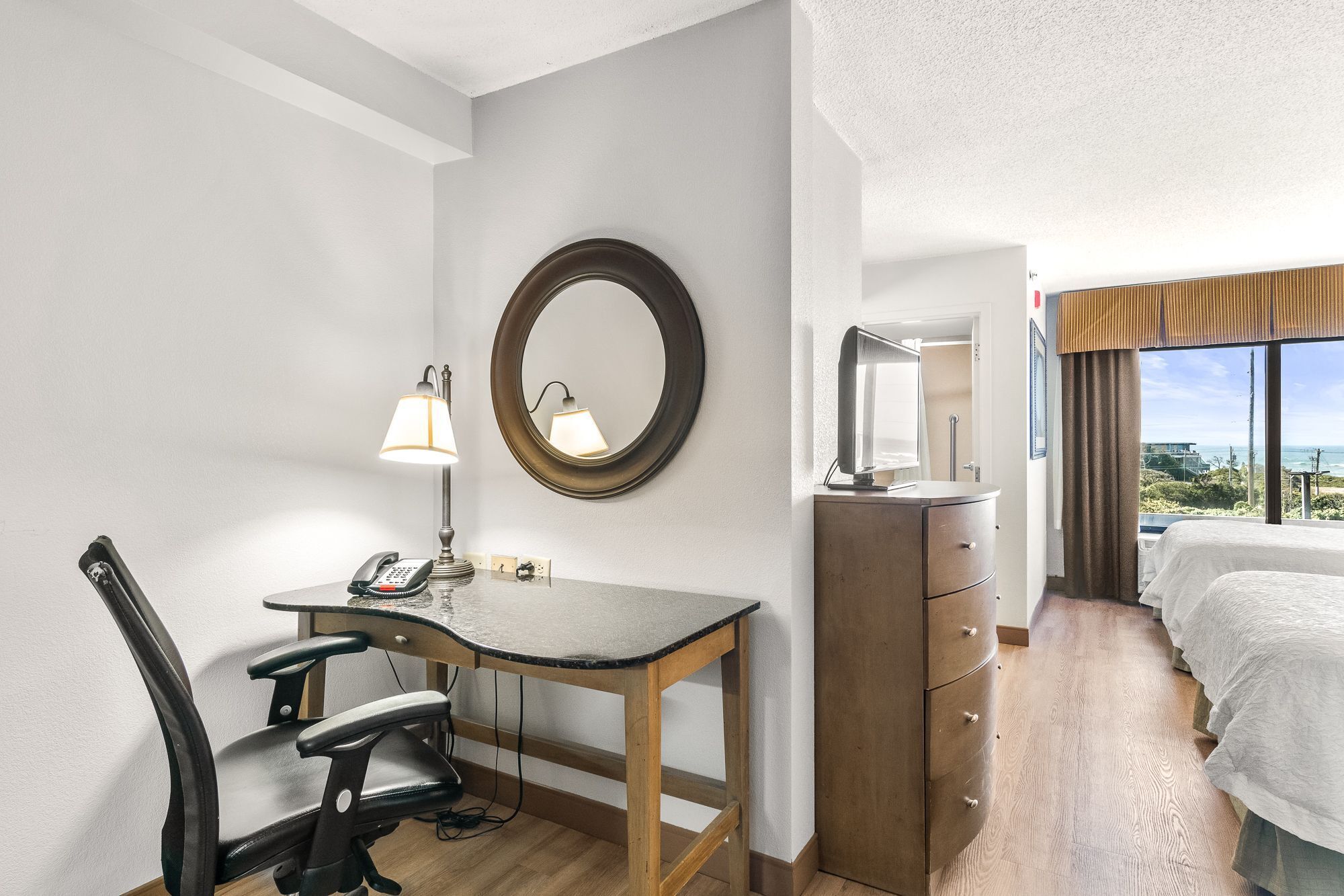 A hotel room with a desk, chair, dresser, and a bed.
