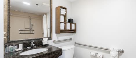 A bathroom with a sink, toilet, and a mirror. There is a towel rack and a shelf with toiletries.