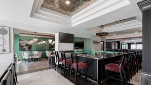 A modern bar area with a marble countertop, black bar stools, and a green accent wall.
