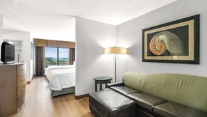 A hotel room with a bed, a sofa, a TV, a lamp, and a framed picture on the wall.