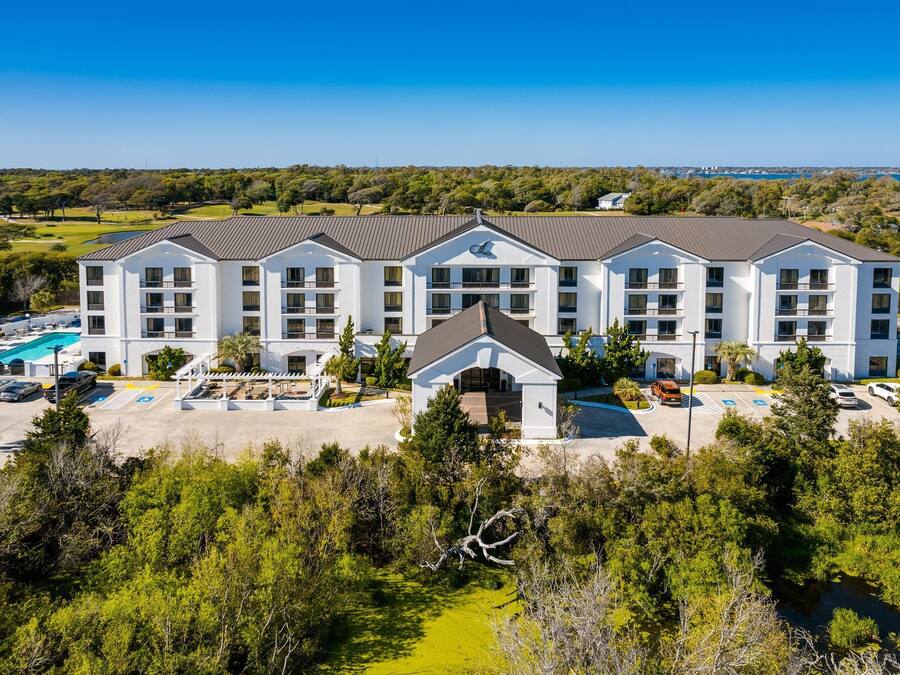 A multi-story hotel with a central entrance, a swimming pool, and a parking area.