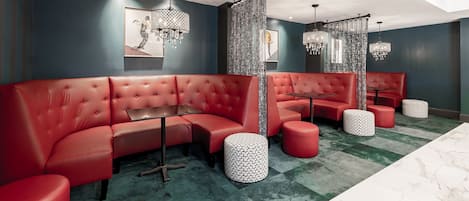 A modern lounge with red leather seating, patterned ottomans, and decorative chandeliers.