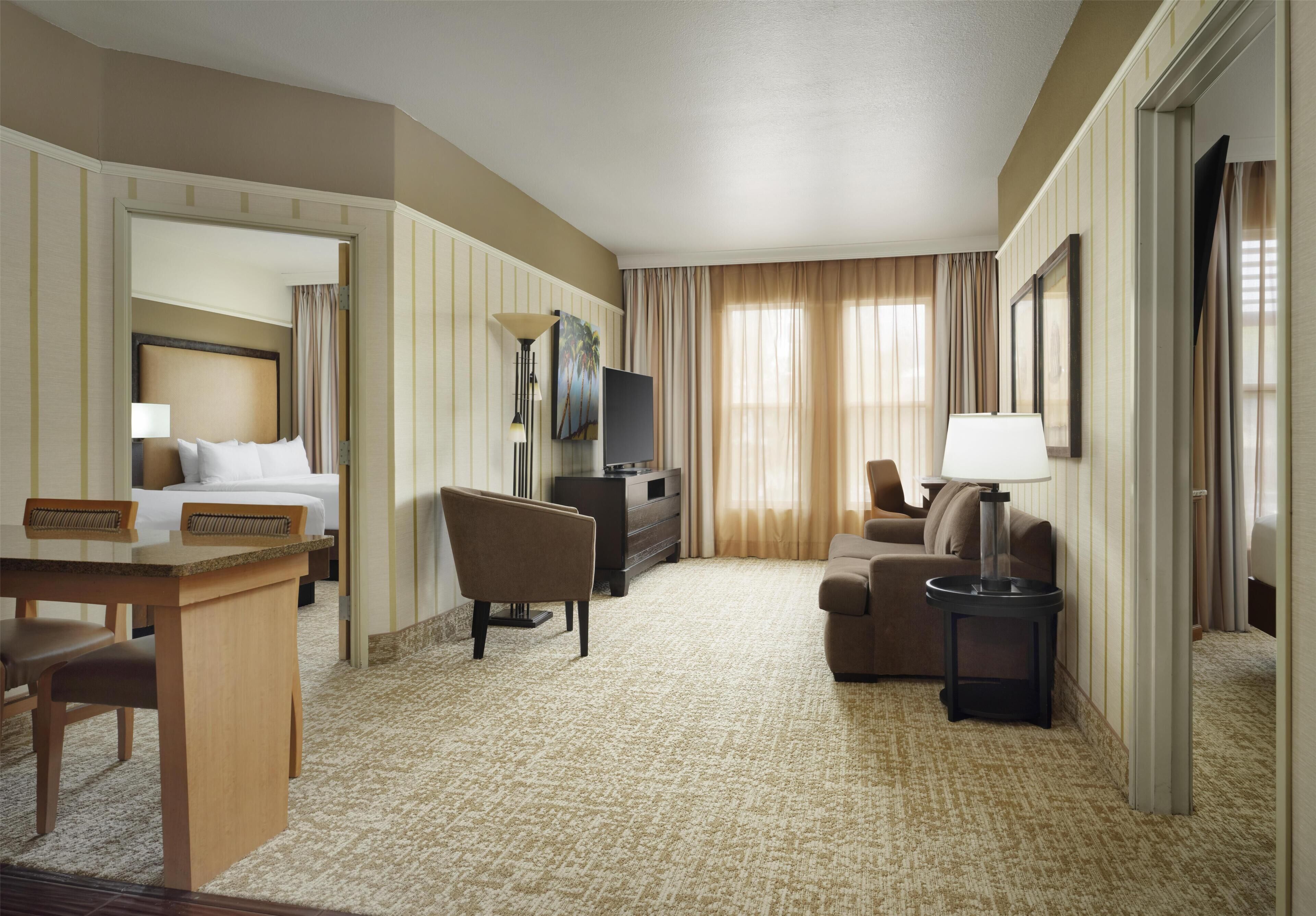 A hotel room with a bed, a desk, a chair, a sofa, a TV, and a lamp.