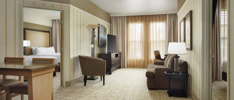 A hotel room with a bed, a desk, a chair, a sofa, a TV, and a lamp.