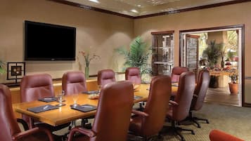 A conference room with a large table, leather chairs, a flat-screen TV, and potted plants.