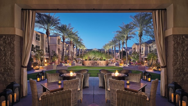 An outdoor dining area with wicker furniture and candles, overlooking a well-maintained garden and buildings. - Sonesta Suites Scottsdale Gainey Ranch (Scottsdale)