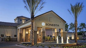 A hotel with a modern design, featuring a prominent entrance, a landscaped garden with a fountain, and palm trees. - Sonesta Suites Scottsdale Gainey Ranch (Scottsdale)