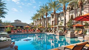 A pool area with lounge chairs and umbrellas, surrounded by palm trees and a building with balconies. - Sonesta Suites Scottsdale Gainey Ranch (Scottsdale)