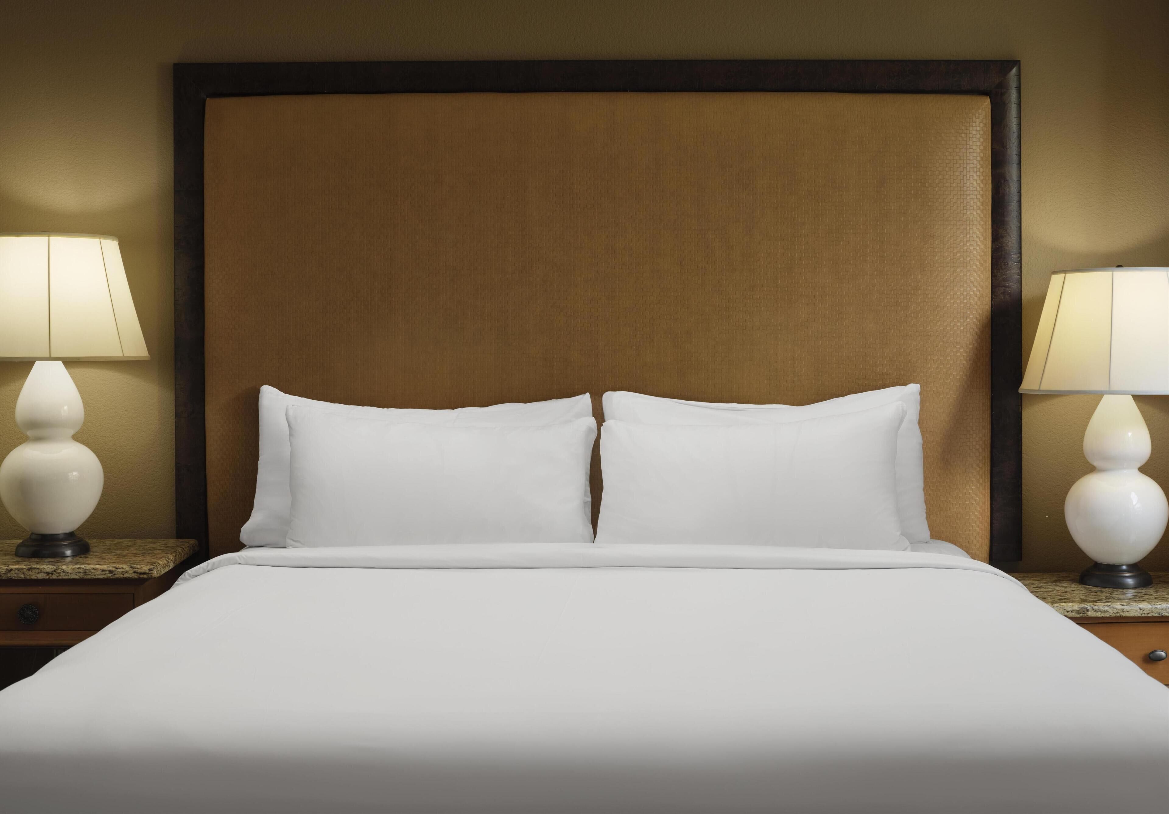 Une chambre d’hôtel avec un grand lit, deux tables de chevet avec des lampes et une tête de lit en bois.