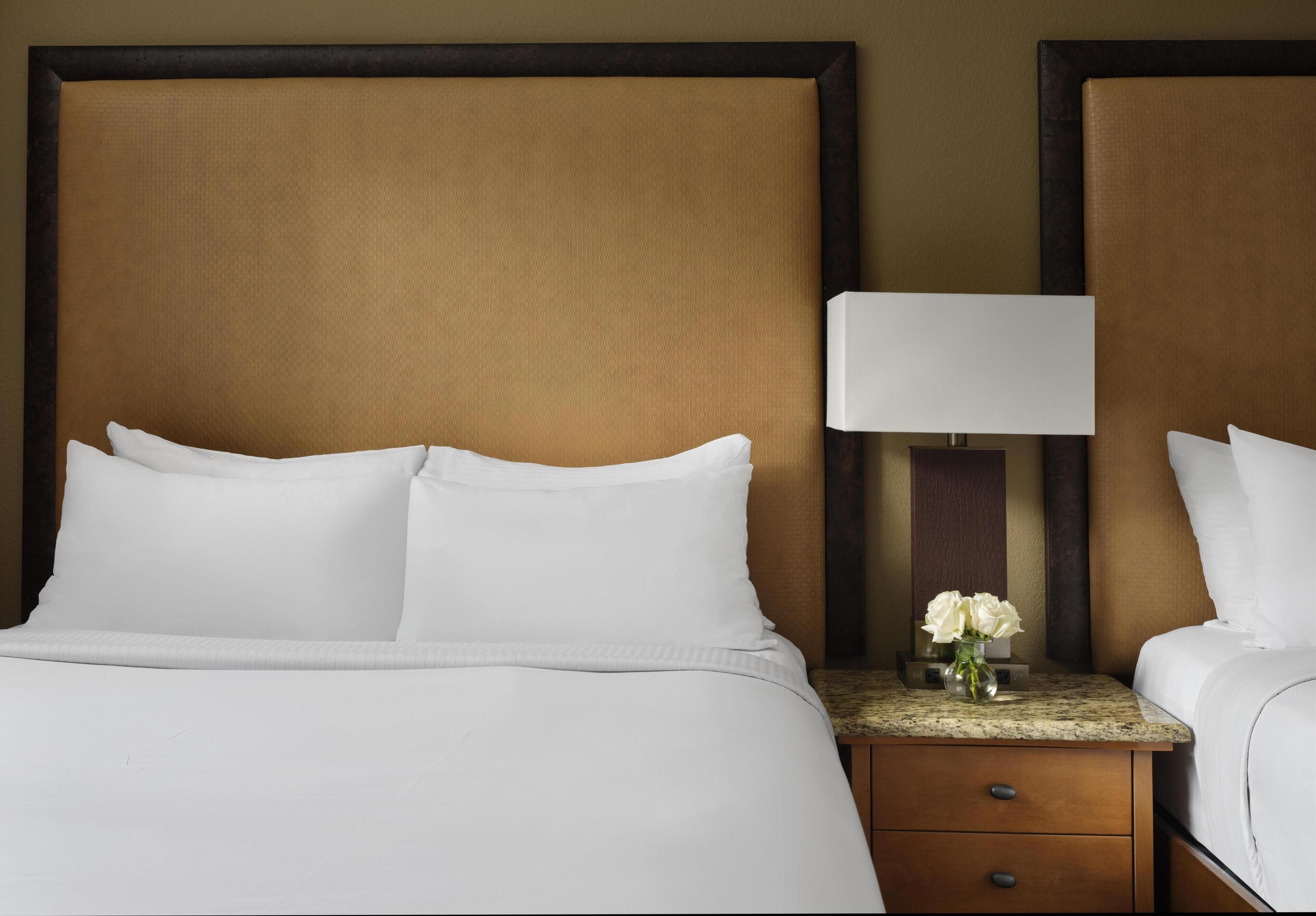 Una camera d'albergo con un letto grande, un comodino con una lampada e un vaso con fiori.