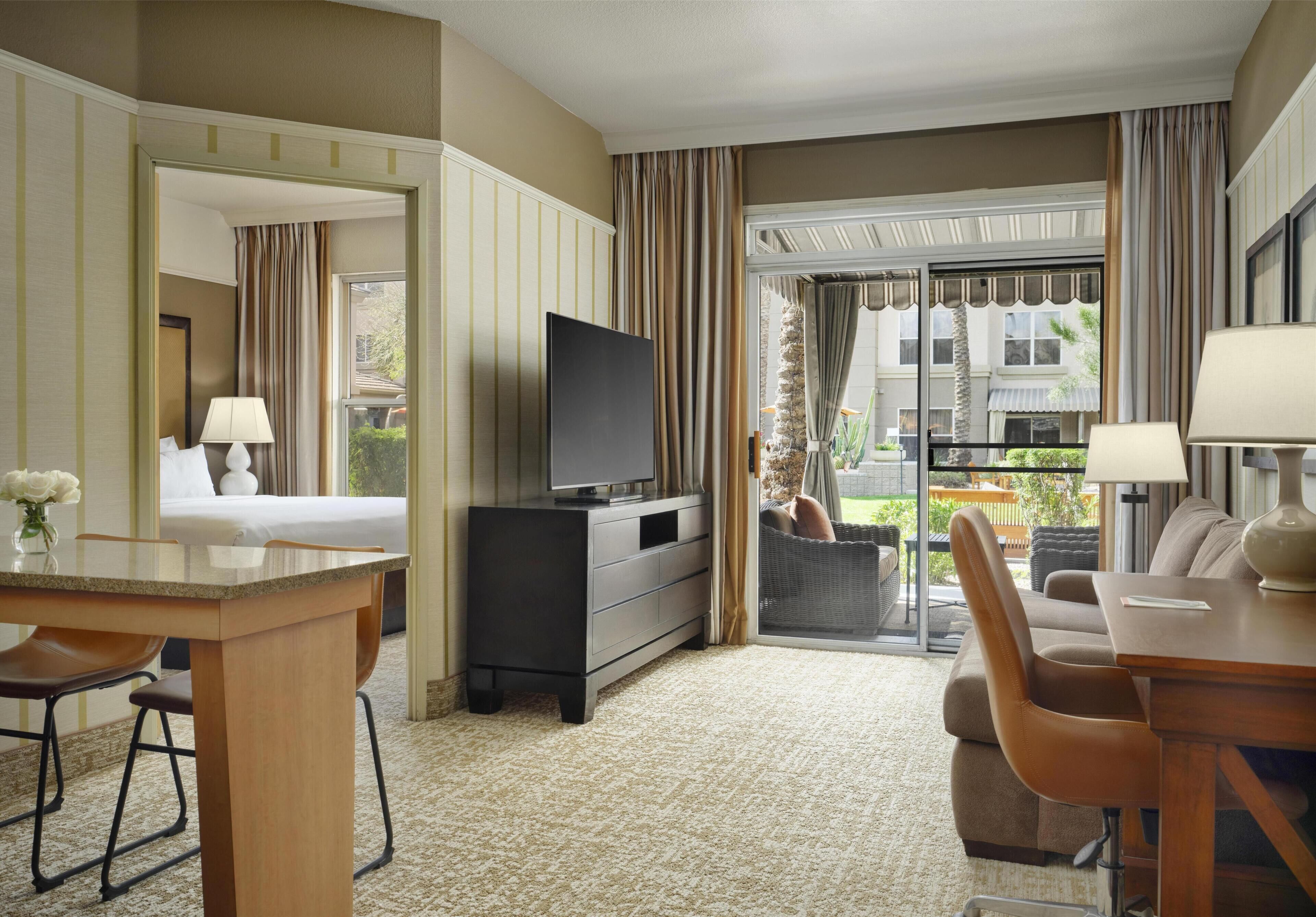 Habitación de hotel con televisión, zona de comedor, sofá y vistas al exterior.