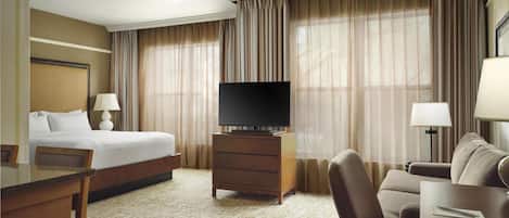 A hotel room with a bed, a TV on a wooden stand, a desk with a chair, a sofa, and a lamp.