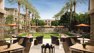 A courtyard with outdoor seating, palm trees, and a central fire feature.