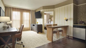 A hotel room with a desk, a chair, a dining table, a TV, a dresser, a mirror, a lamp, a rug, and a dishwasher.