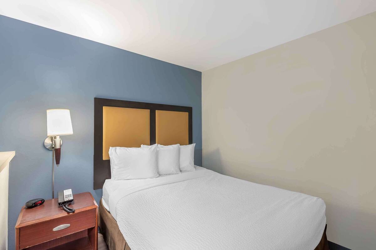 A hotel room with a bed, a nightstand with a lamp, and a phone.