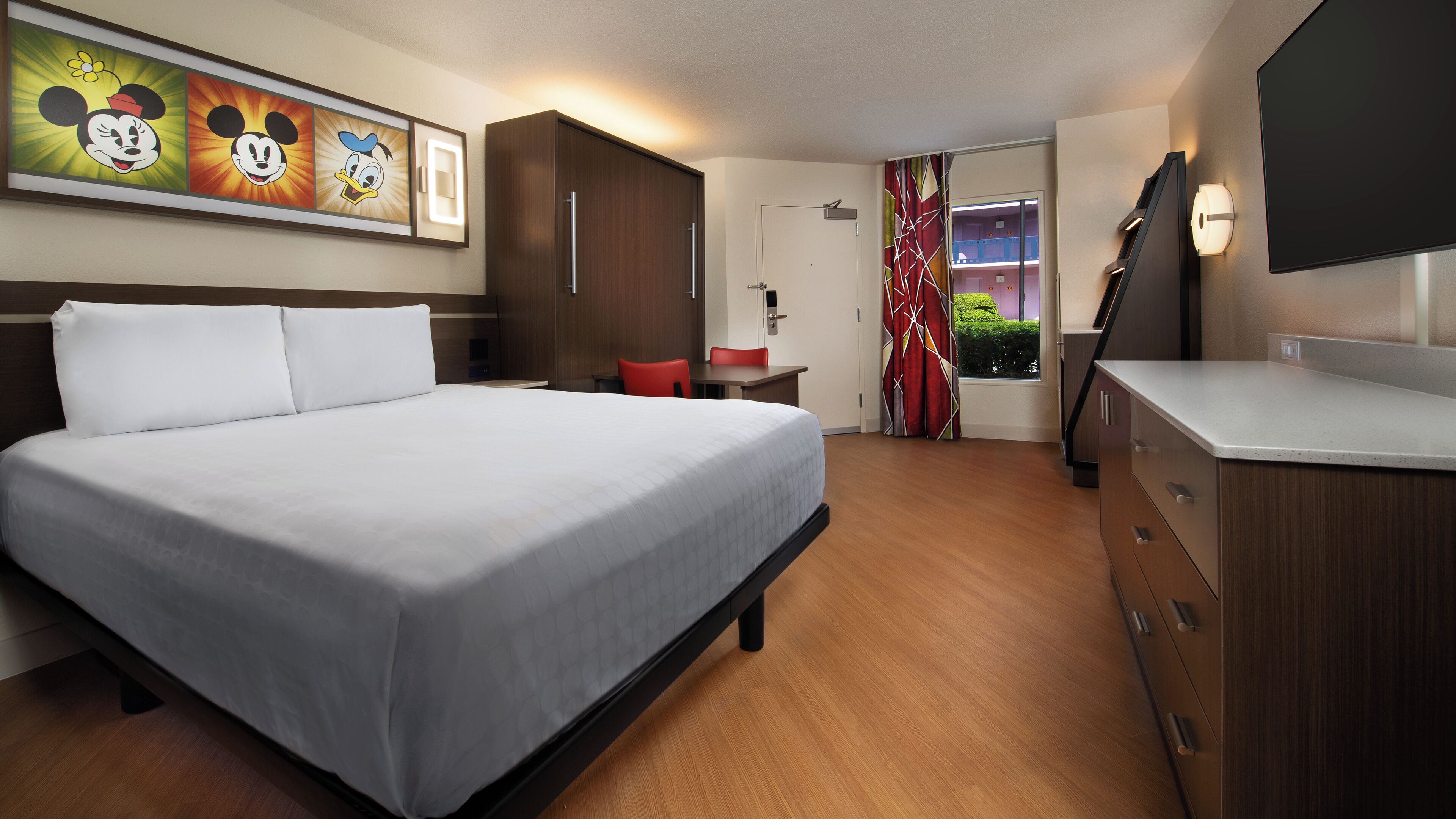 Camera d'albergo con un letto grande, una scrivania, una sedia, una TV e una finestra con tende.
