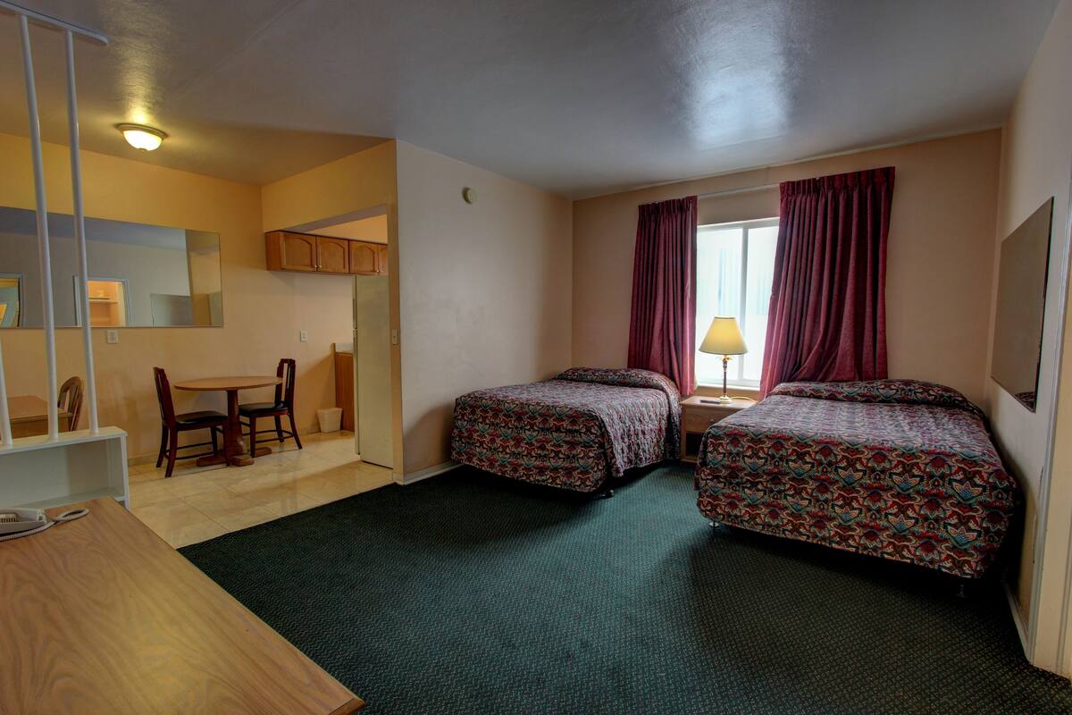 Une chambre avec deux lits simples, un bureau en bois, une chaise, une petite table et un miroir.