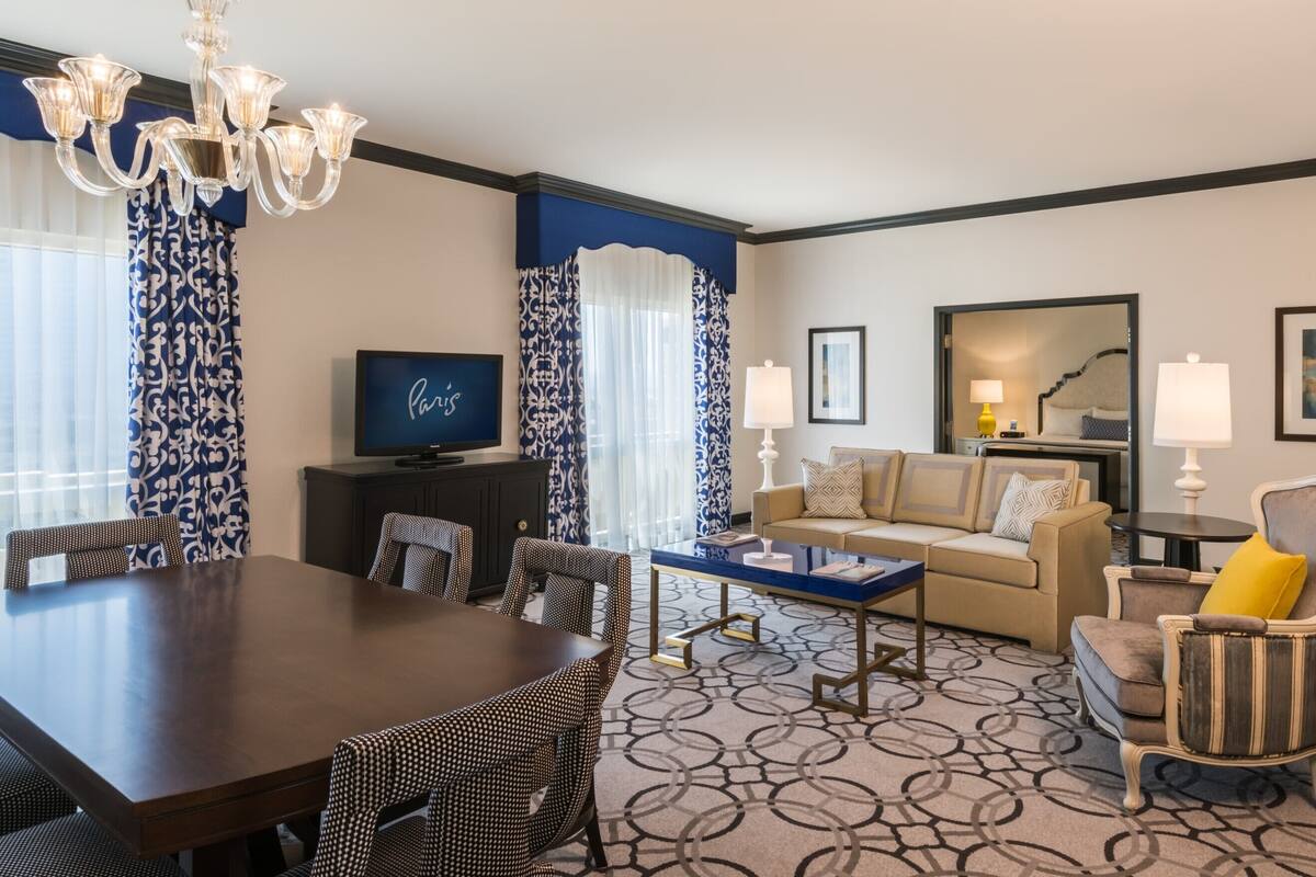 Habitación de hotel con una mesa de comedor, sillas, un sofá, un televisor y una alfombra estampada.