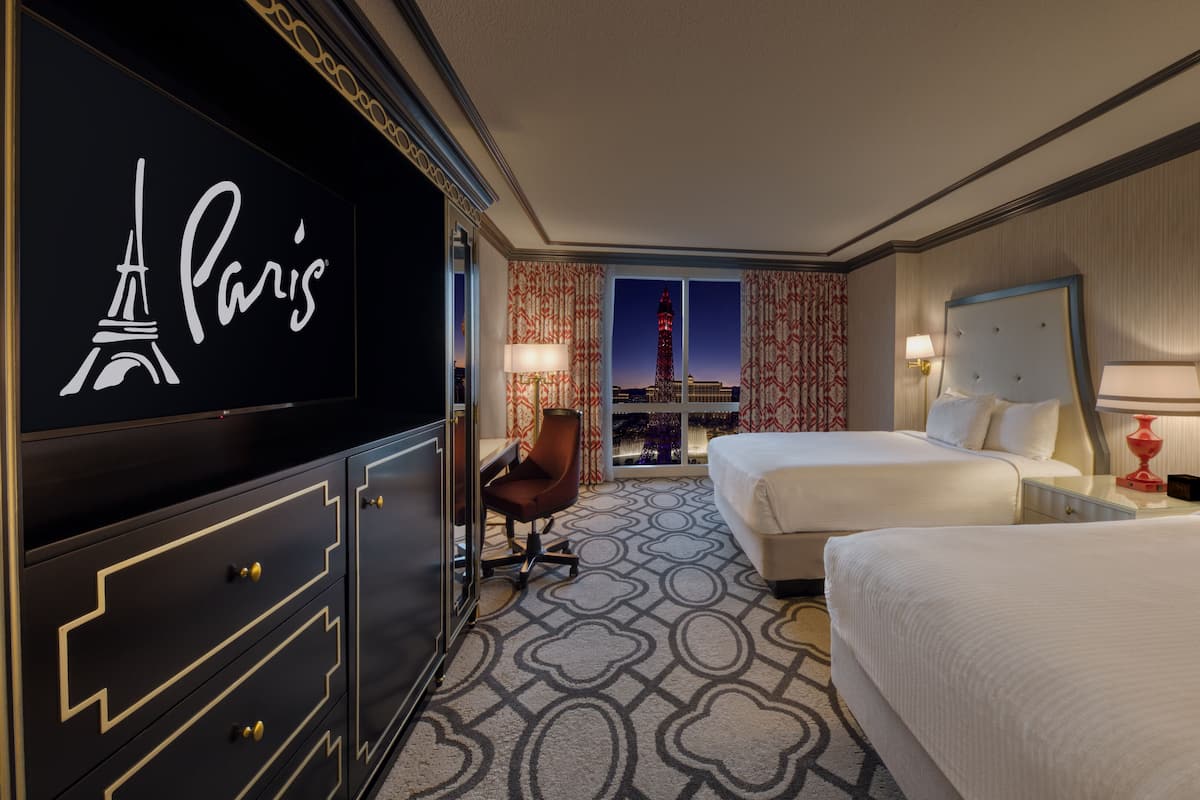 Habitación de hotel con dos camas, un televisor mostrando la Torre Eiffel y vista nocturna de la Torre Eiffel.
