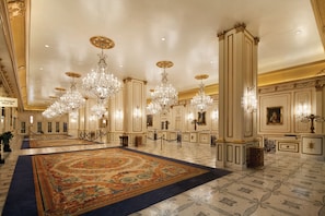 A grand lobby with ornate chandeliers, a large patterned carpet, and classical columns.