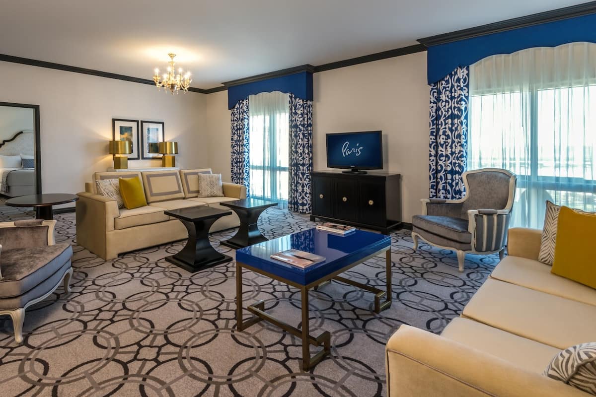 Habitación de hotel moderna con sofá, sillones, una mesita de centro, televisión y una araña.