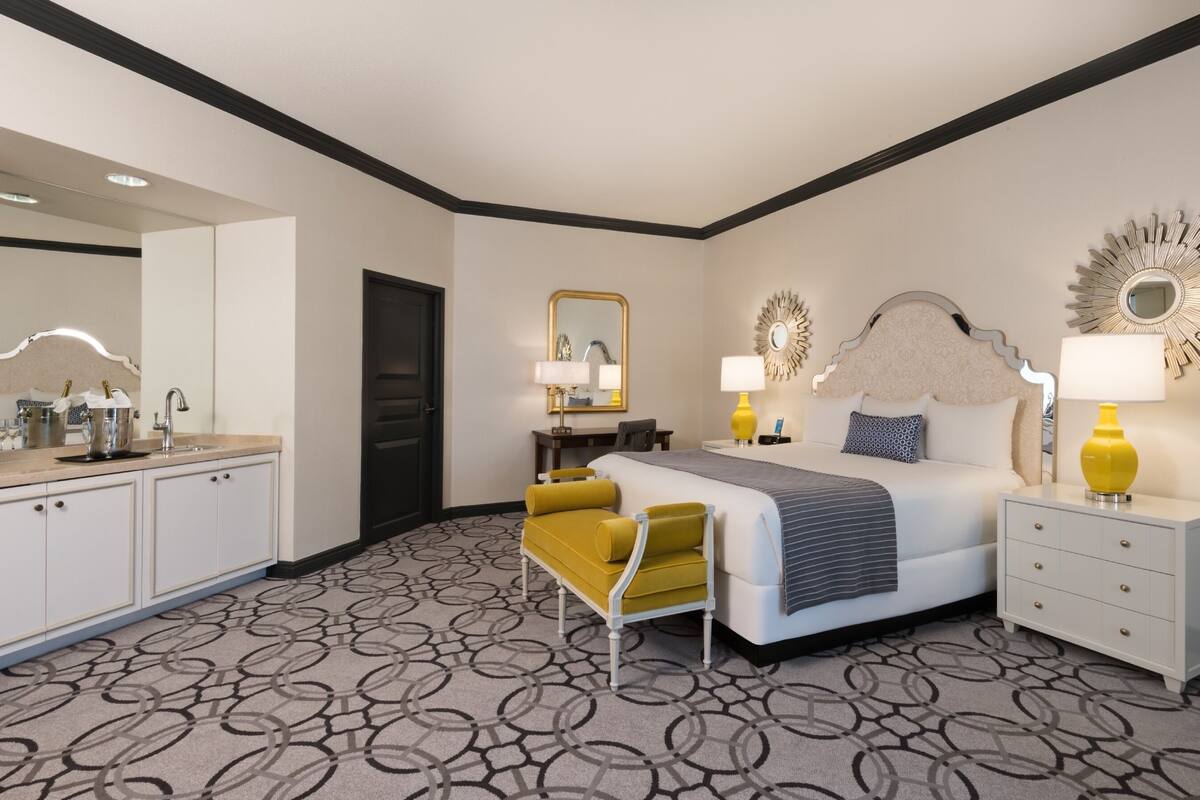 Habitación de hotel con cama, mesitas de noche, escritorio, silla, espejo y baño con lavabo e inodoro.