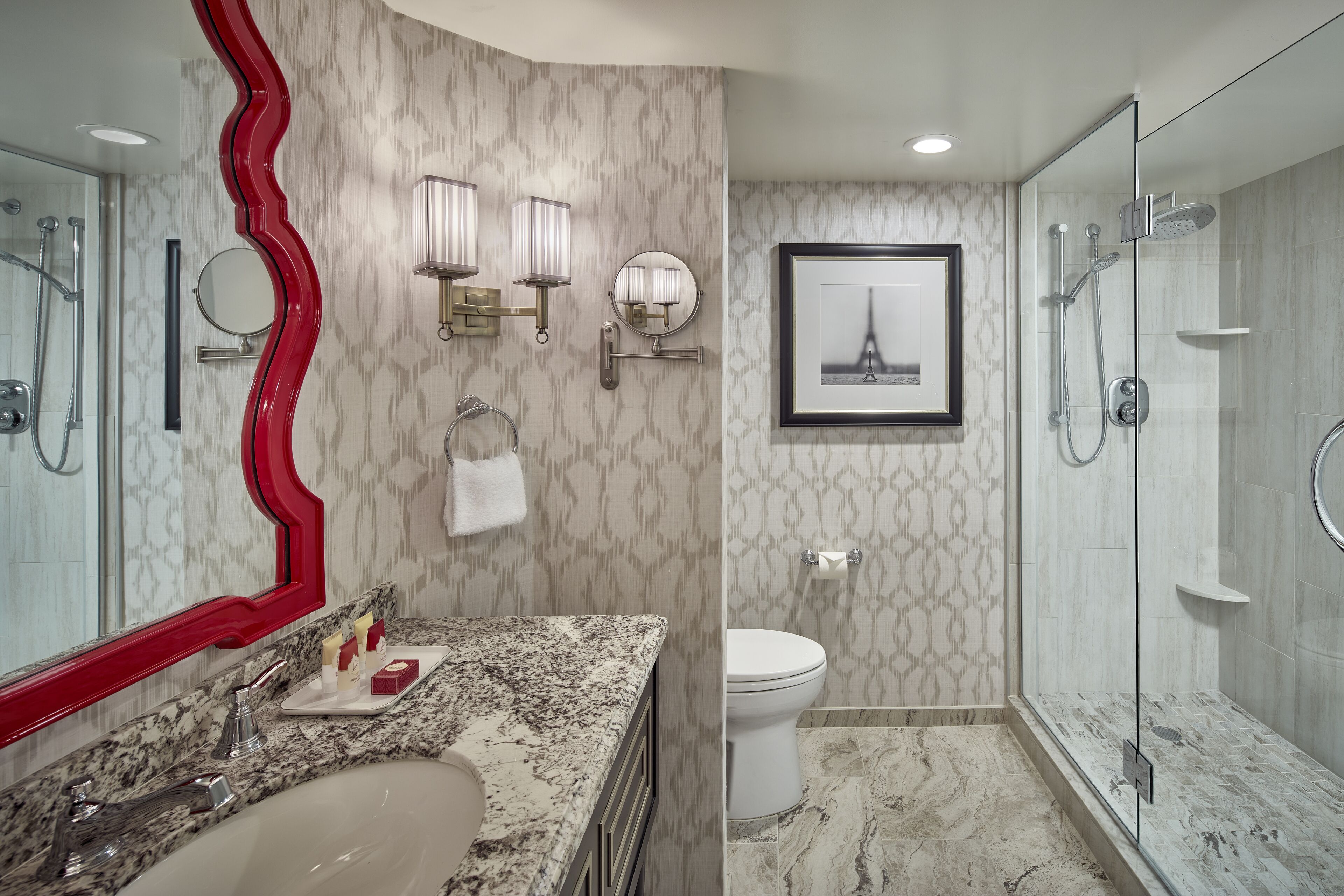 A modern bathroom with a marble sink, a large mirror, a framed picture of the Eiffel Tower, and a glass-enclosed shower.