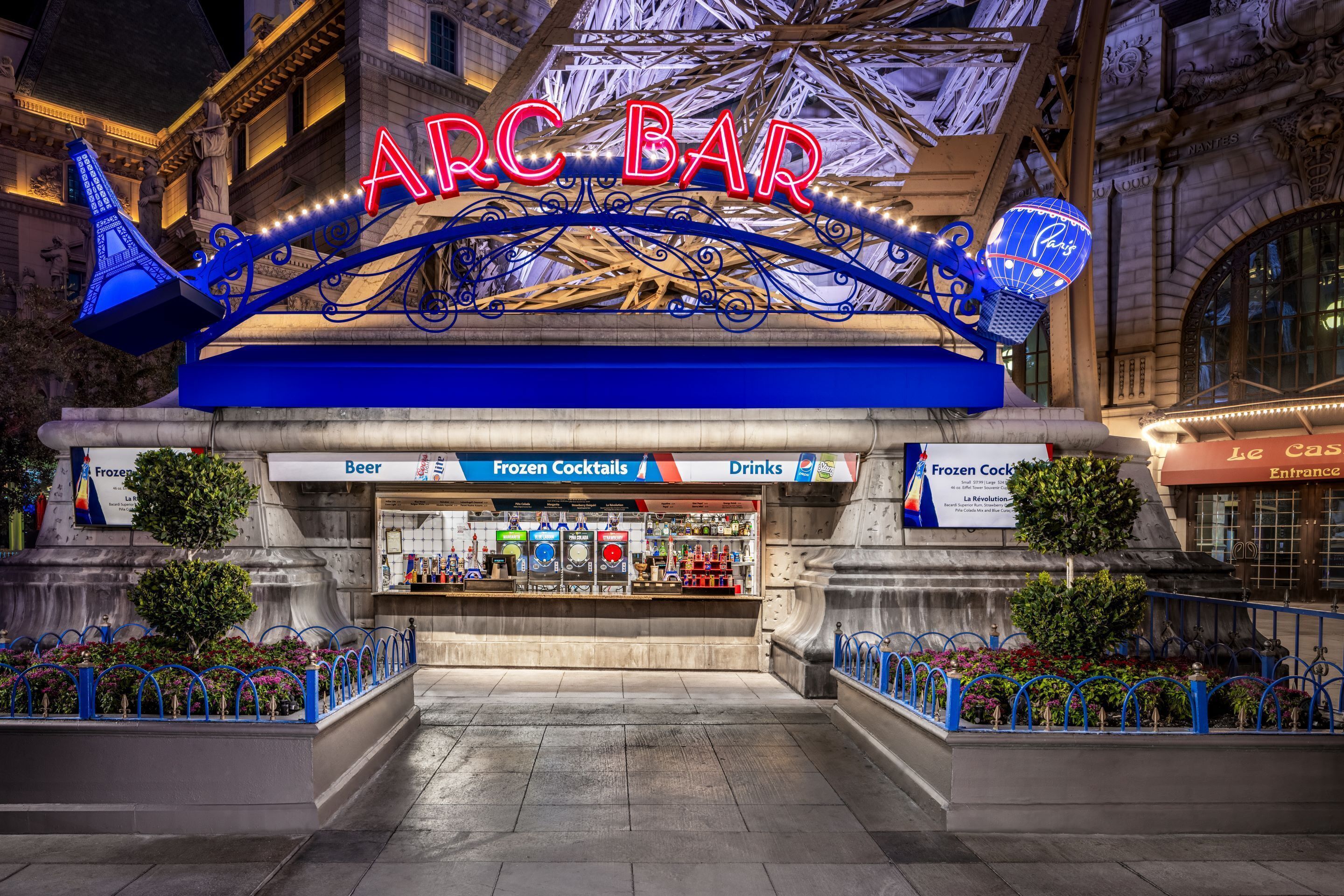 Un bar tipo arcade con letreros de neón, una sección de cócteles helados y una entrada con temática parisina.