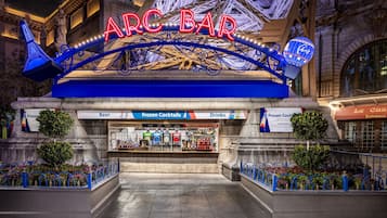 Un bar tipo arcade con letreros de neón, una sección de cócteles helados y una entrada con temática parisina.