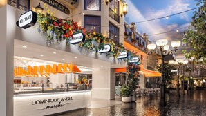 Une rue mouillée avec un restaurant appelé « DOMINIQUE ANSEL marchi » et des panneaux indiquant « GLACES », « PLAT CUIT AU FOUR », « SANDWICHS » et « CRÊPES ».