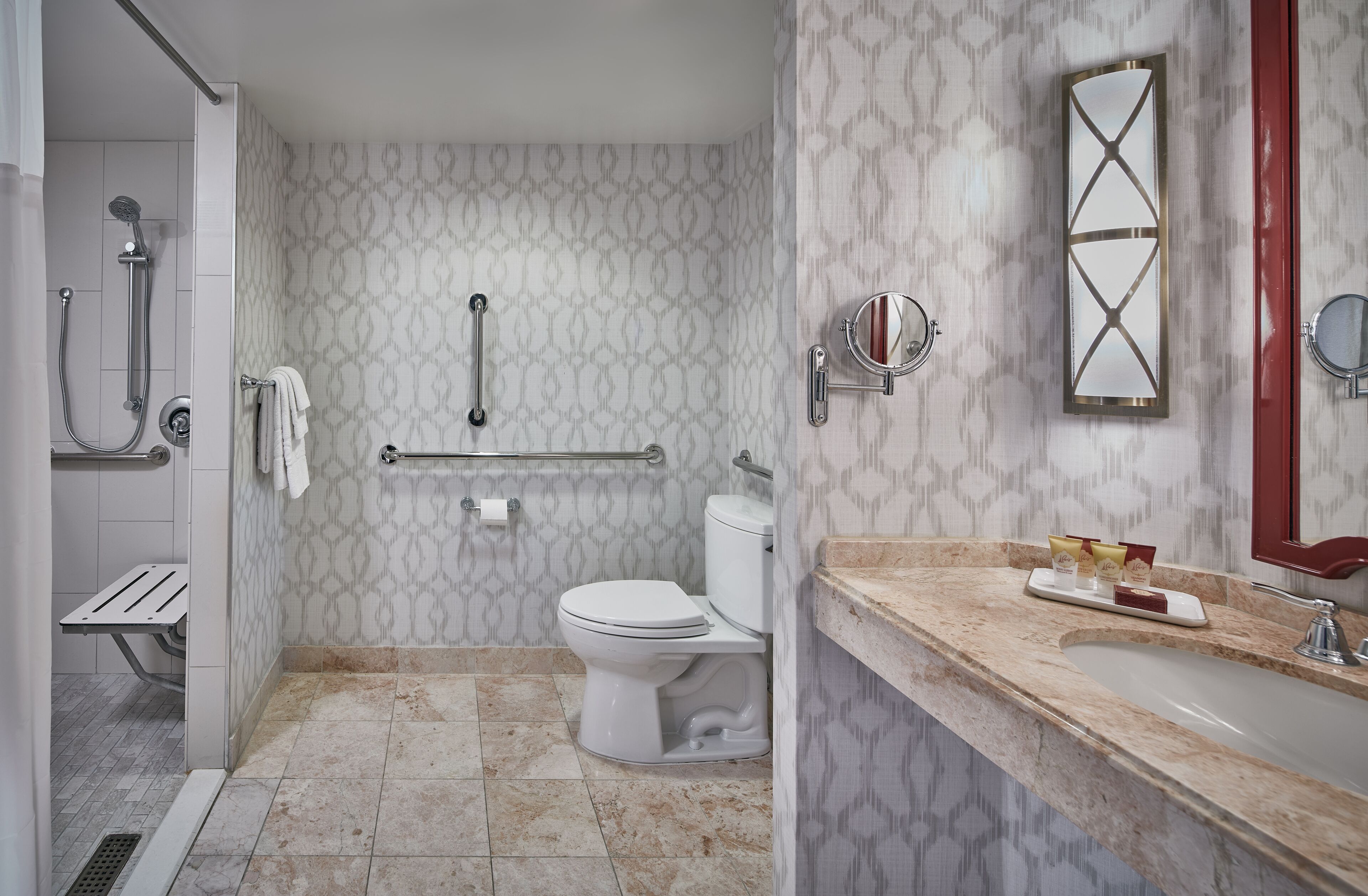 Un baño equipado con inodoro, ducha, barras de apoyo, toallero, lavabo y espejo.