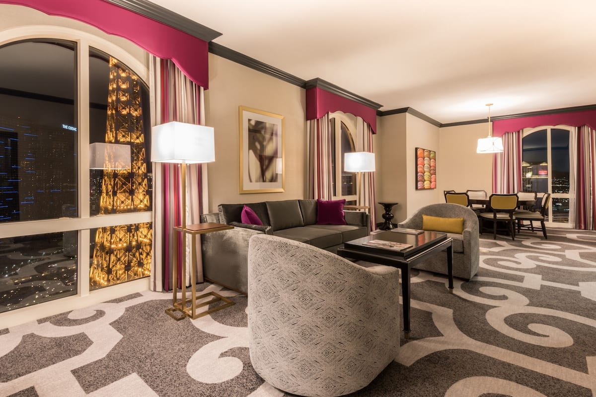 Una habitación de hotel moderna con un ventanal grande, un sofá, una silla, una mesa de centro y un comedor.