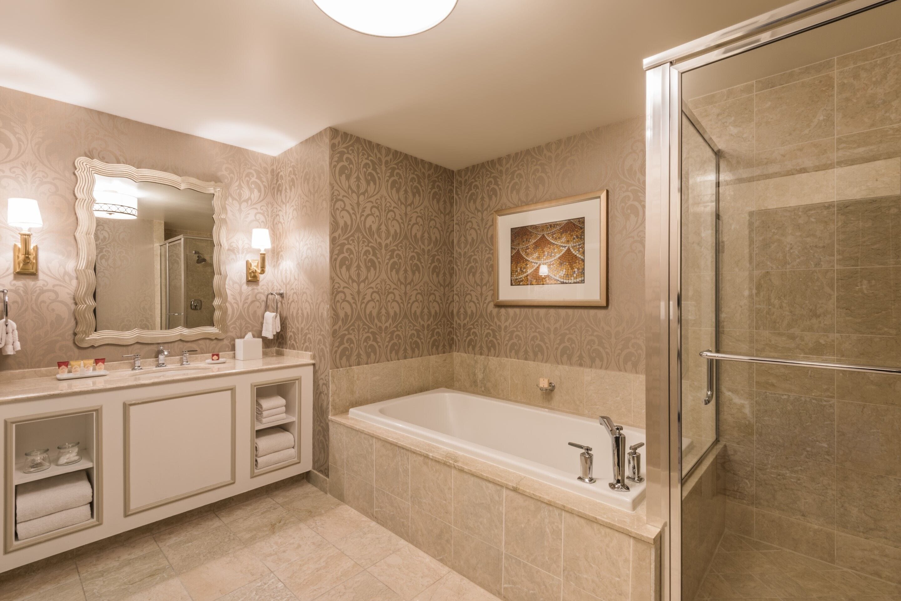 A bathroom with a large mirror, a bathtub, a shower, and a vanity with a sink and towel racks.