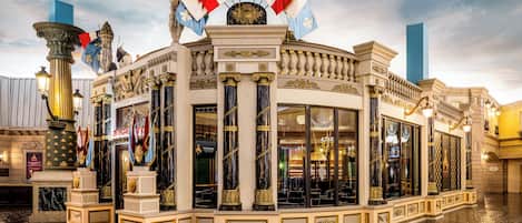 Un imposant bâtiment aux colonnes richement décorées et aux drapeaux, doté de grandes fenêtres et d’un sol réfléchissant.