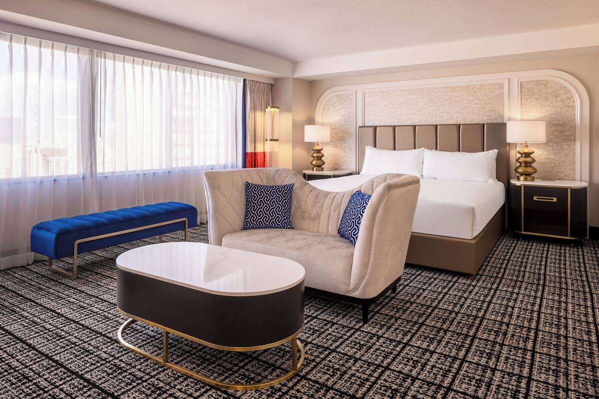 Una habitación de hotel con una cama, un sofá, una mesita y un banco.