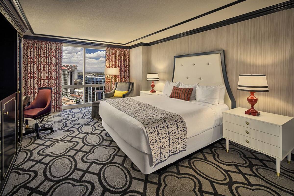 Habitación de hotel con una cama grande, un escritorio, una silla y vistas a la ciudad.