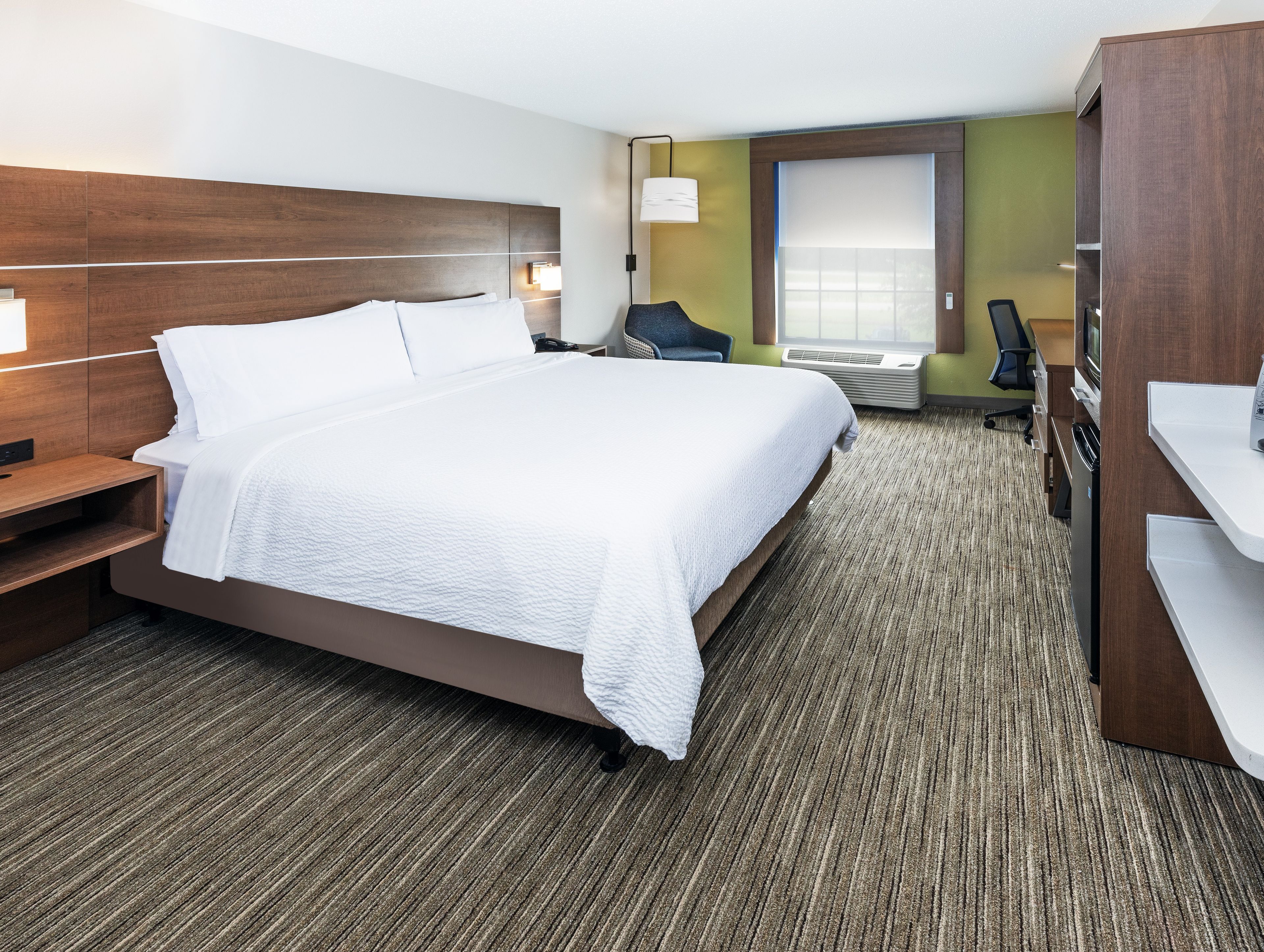 A hotel room with a large bed, a desk, a chair, a TV, and a window with blinds.