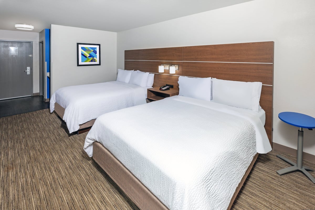 A hotel room with two beds, a wooden headboard, a small table, and a framed picture on the wall.