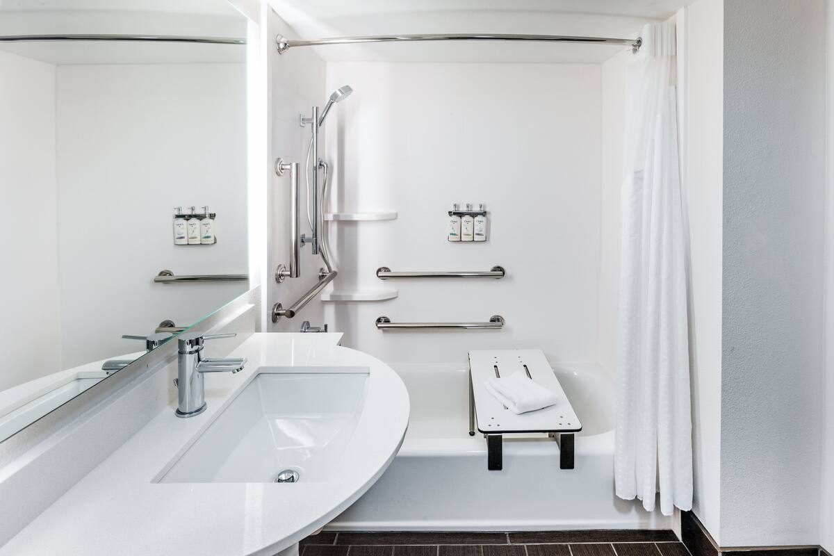 A modern bathroom with a large sink, a shower with a glass door, and handrails.