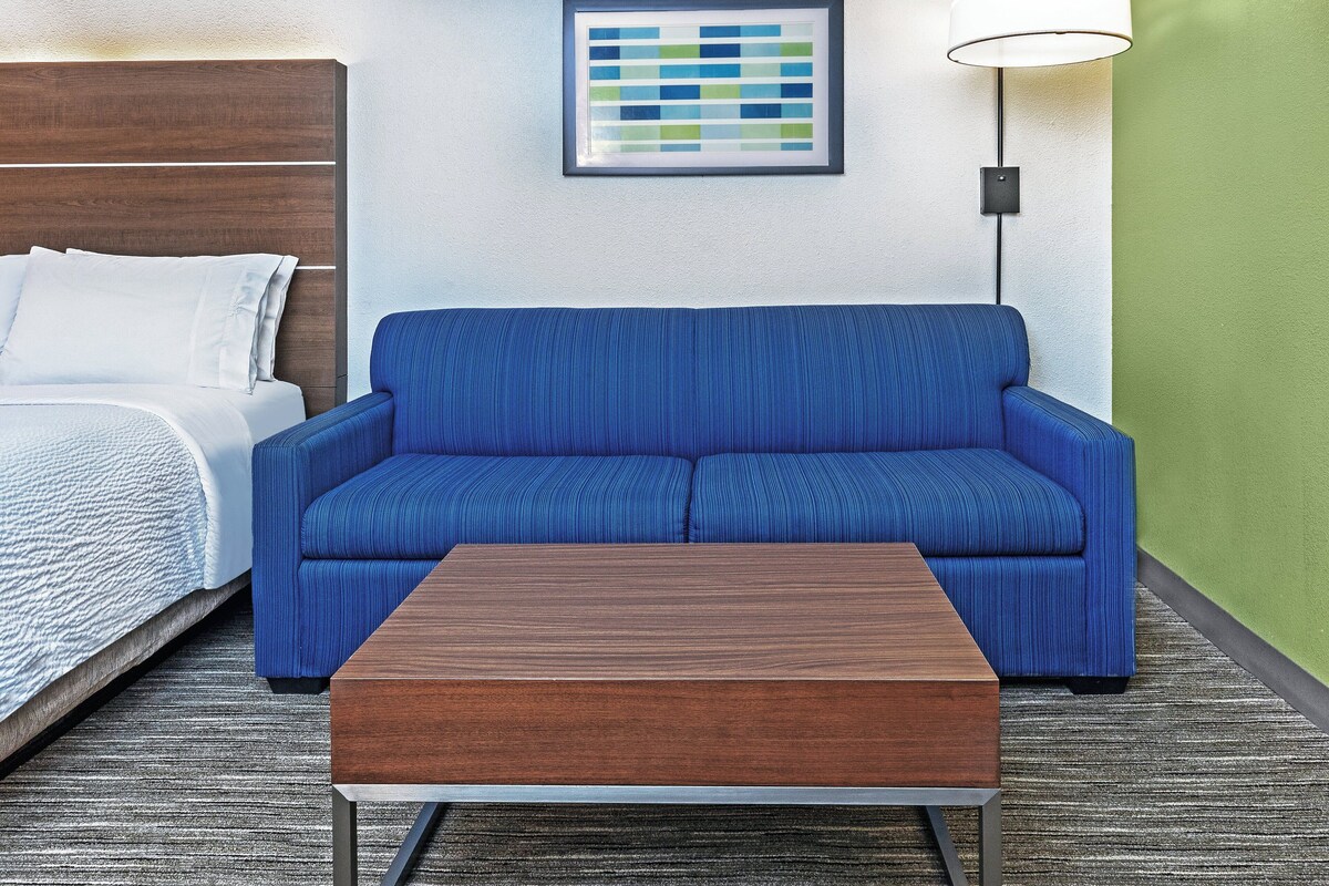 Una habitación de hotel con una cama, un sofá azul, una mesa de centro de madera y una obra de arte enmarcada en la pared.