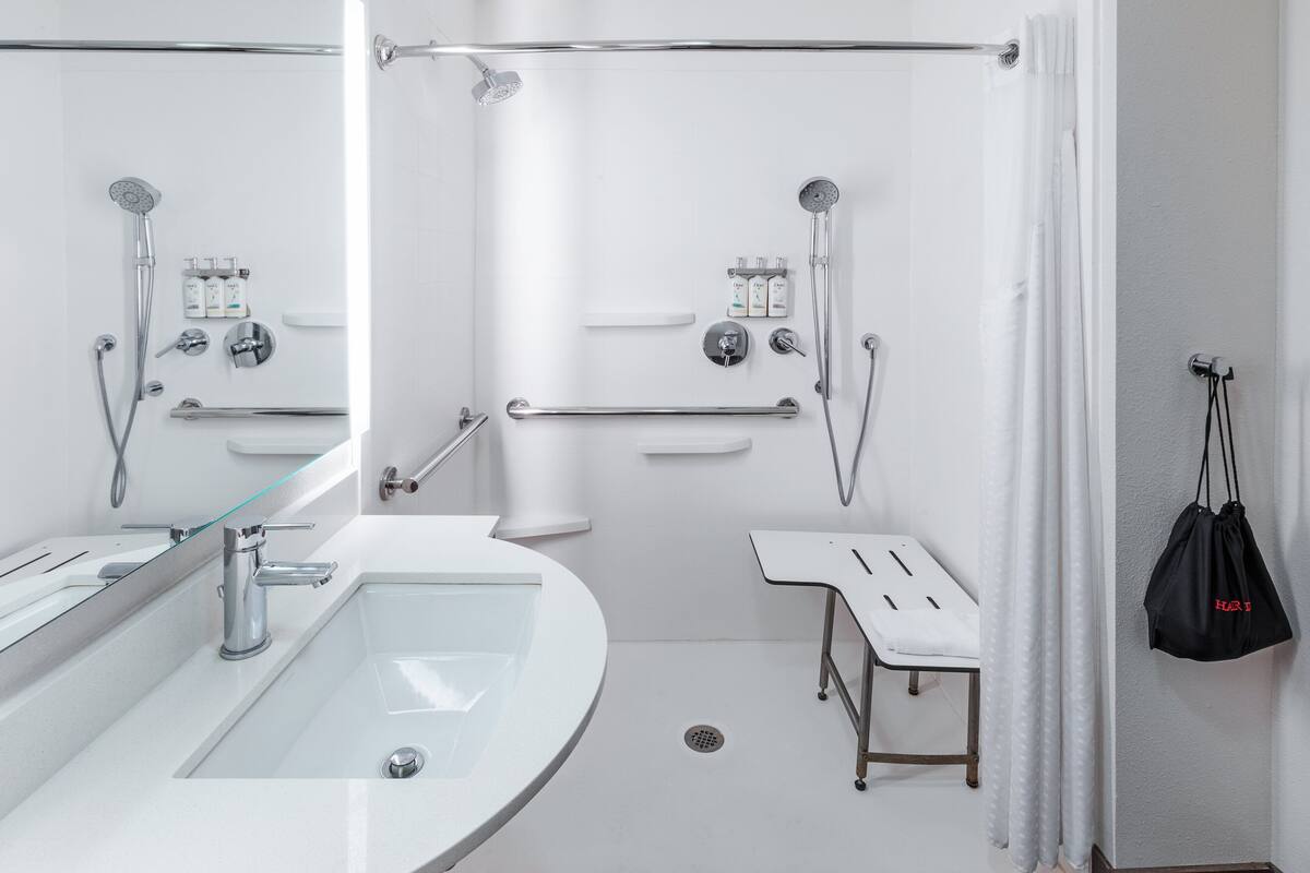 A modern bathroom with a glass-enclosed sink, a shower with a handheld showerhead, and a grab bar.