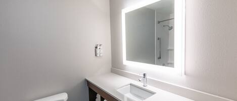 A bathroom with a toilet, a sink, a mirror, and a shower.