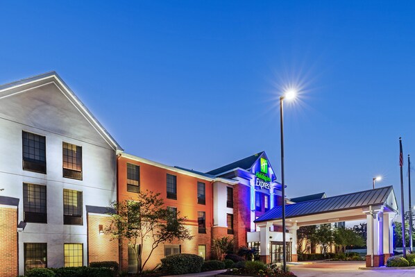 Un hotel Holiday Inn Express con un diseño moderno, que presenta una combinación de paredes exteriores de ladrillo y blancas, y un área de entrada bien iluminada.