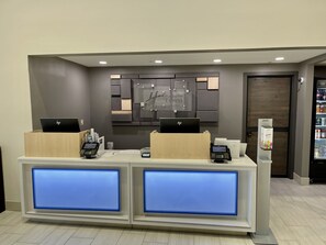 A hotel reception desk with two HP laptops, a digital display, and a Cintas self-service kiosk.