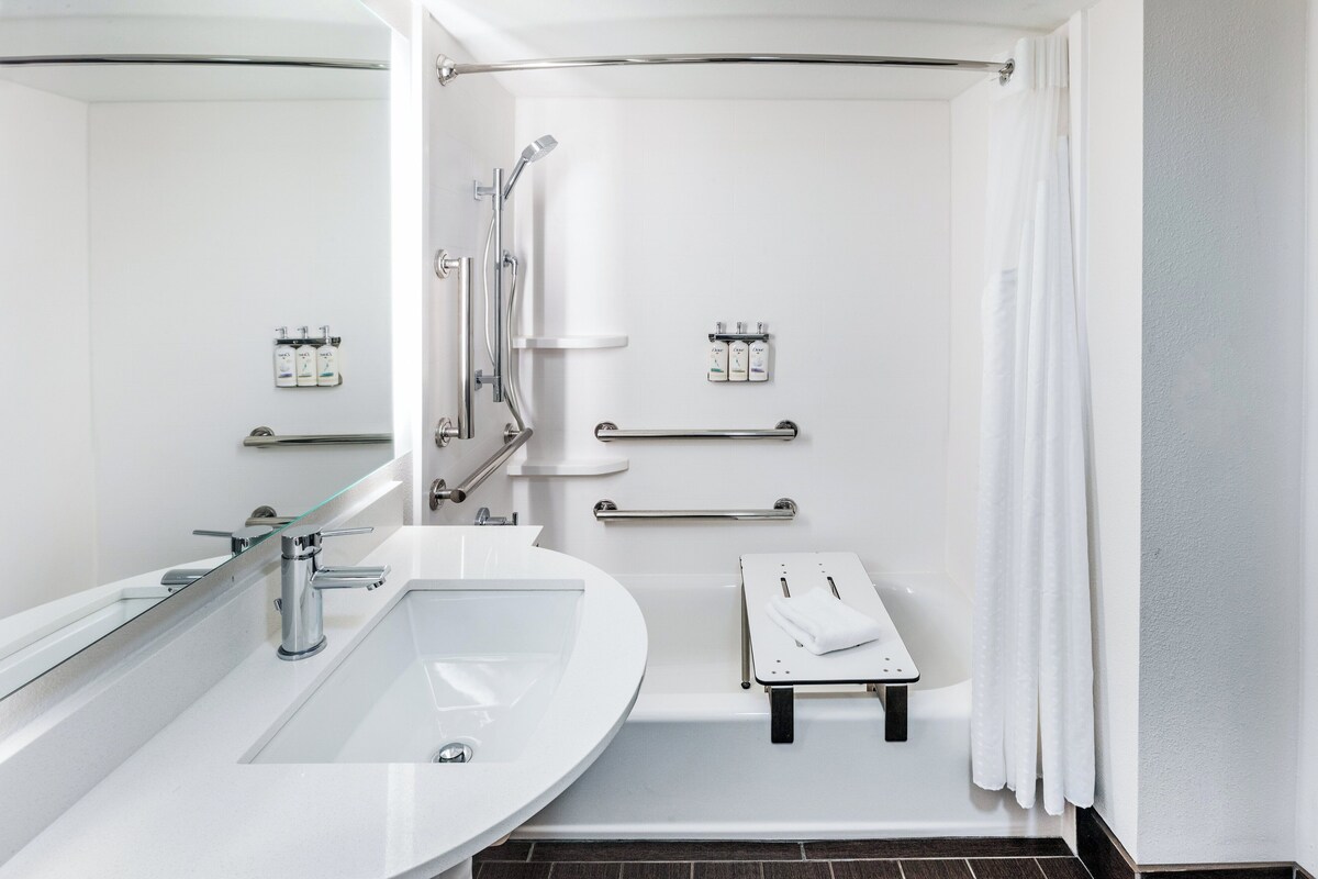Un baño moderno con un lavamanos grande, ducha con puerta de vidrio y barras de apoyo.