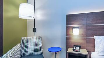 A hotel room with a bed, a small table with a telephone, a sofa, and a lamp.
