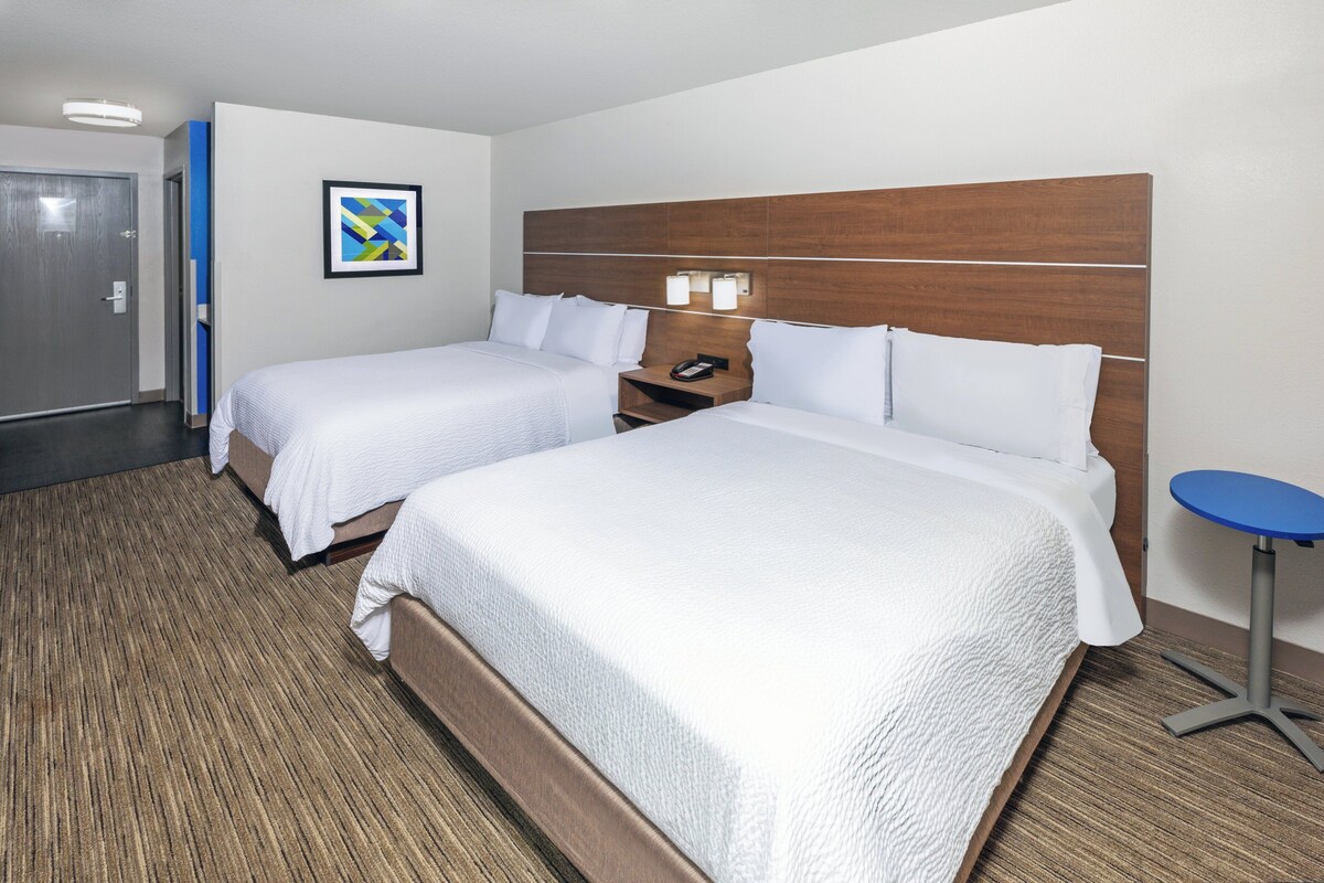 Habitación de hotel con dos camas, cabecero de madera, una mesita y un cuadro enmarcado en la pared.